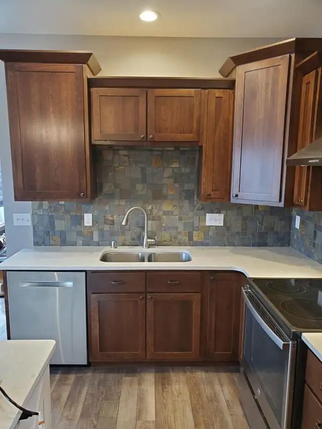 Cherry shaker kitchen cabinets with a slate tile backsplash, white countertops and a double sink