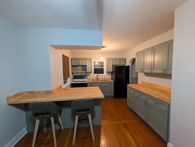 Kitchen with gray cabinets, wood countertops and a breakfast bar with two stools