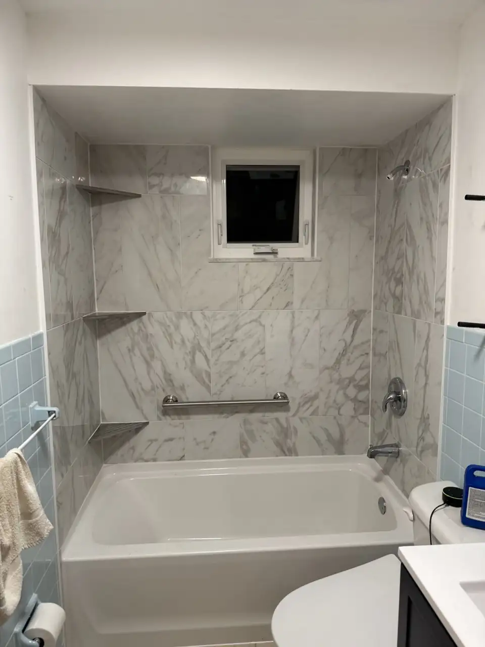 Tub surround by a bathroom remodeler in Sharpsville: large white marble-look tile, corner shelves, a grab bar and a new tub under a small window