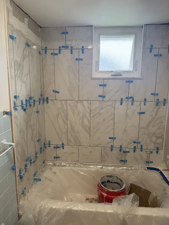 Large marble-look wall tile being set with blue leveling clips around a tub and window