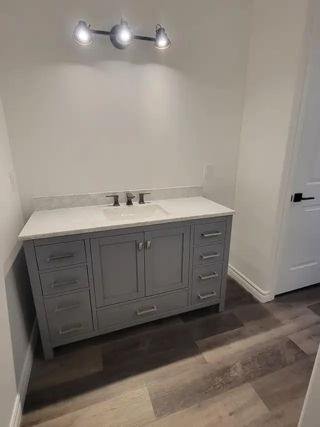 New gray shaker bathroom vanity with a white top and brushed nickel faucet against a freshly painted white wall
