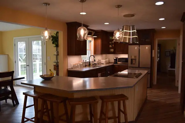 Kitchen with dark cherry cabinets, an angled island with cooktop and beadboard sides, glass pendant lights and a white subway tile backsplash